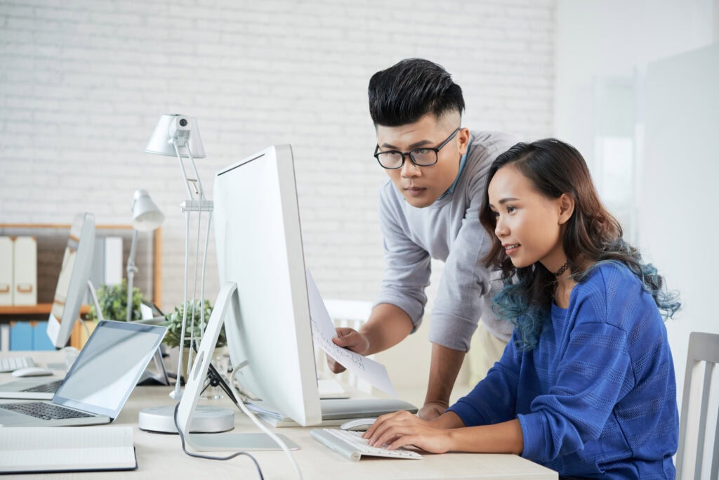 Modern professionals collaborating at a desk with multiple computers in a bright office space.