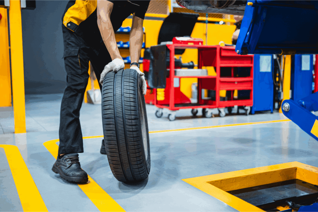 Tire maintenance worker handling a car tire in an industrial workshop, emphasizing auto service and repair.