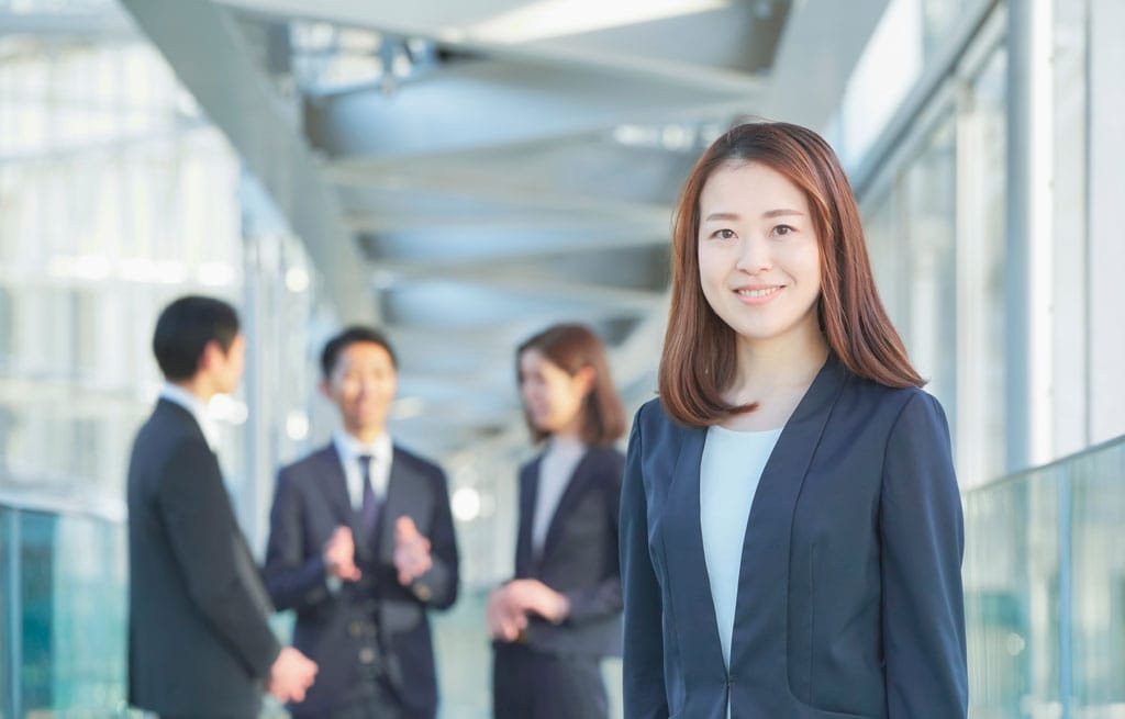 Professional businesswoman smiling at conference with colleagues in background.