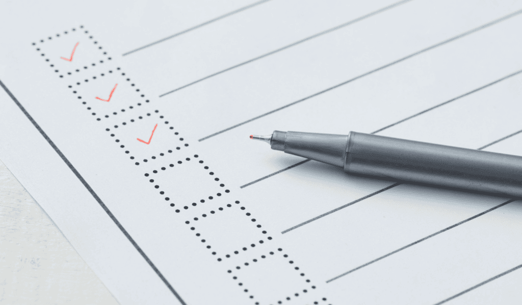 Close-up of a checklist with red checkmarks and a silver pen on paper.