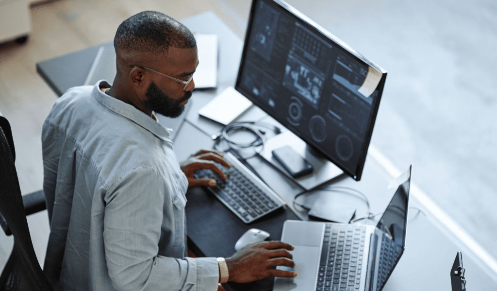 Business analyst working on data analytics on dual monitors in modern office.