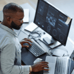 Business analyst working on data analytics on dual monitors in modern office.